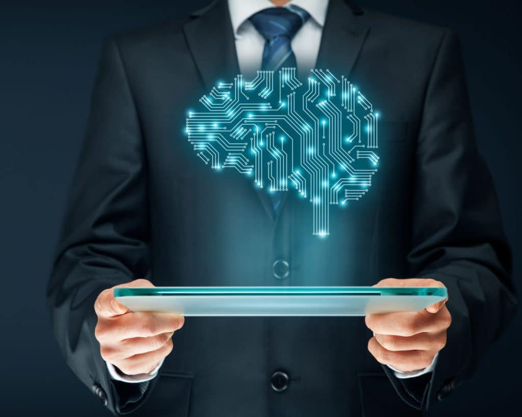 An image of someone holding a tablet. Above the tablet is a hologram of a human brain.