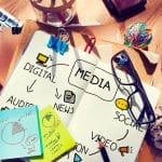 An image of clutter desk. In the center is a rough marketing plan drawn on a note book.