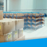 An image from inside a warehouse. It shows order items stacked in the foreground and tidy aisles in the background.