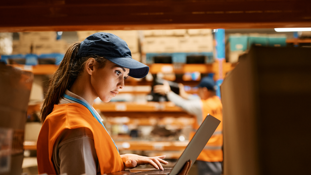 An image showing a warehouse worker checking something on a laptop.