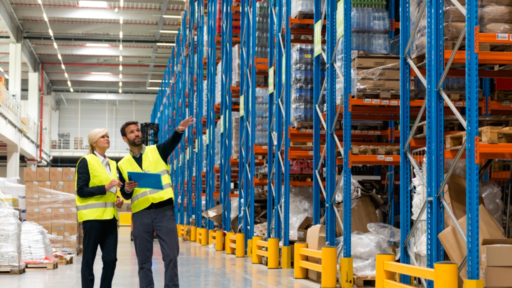 An image showing two warehouse workers. One points to one of the aisles in the distance. They seem to be planning something.